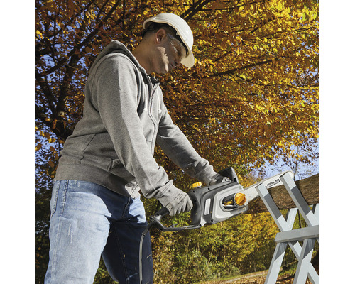 Mann mit Schutzhelm und Schutzbrille sägt Holz mit einer Kettensäge.