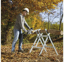 Mann sägt Holzscheit mit einer Kettensäge auf einem Sägebock im Freien