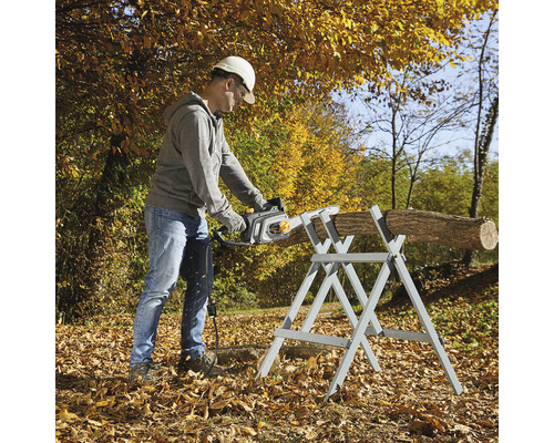 Mann sägt Holzscheit mit einer Kettensäge auf einem Sägebock im Freien