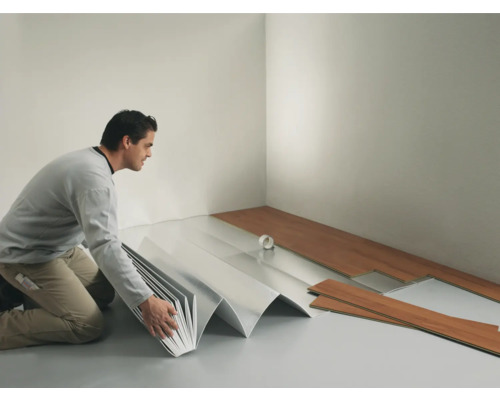 Ein Mann verlegt Laminatboden in einem Raum mit Trittschalldämmung.