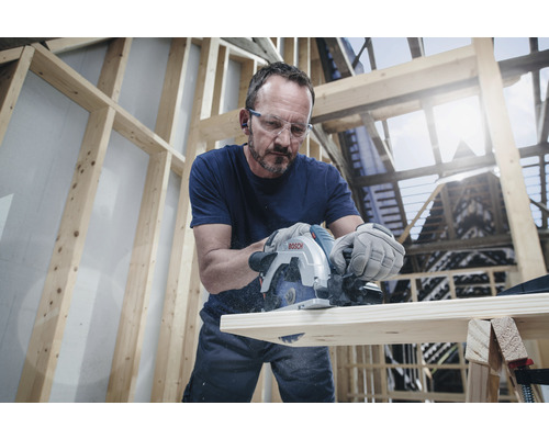Un homme scie une planche de bois avec une scie plongeante Bosch dans un atelier lumineux.