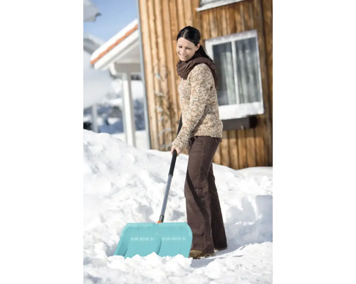 Une femme déblaie la neige avec une pelle à neige devant une maison.