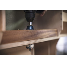 Une perceuse perce un trou dans une planche de bois.