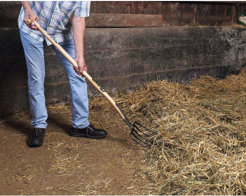 Une personne utilise une fourche à foin pour déplacer du foin.
