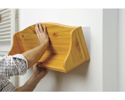 Mann befestigt ein Wandregal aus Holz an einer Wand