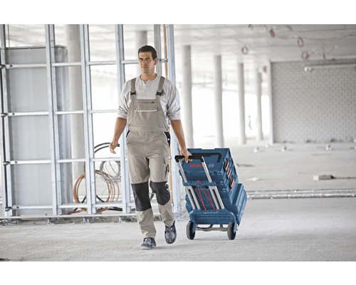 Handwerker zieht einen Werkzeugkoffer mit Rollen der Marke Bosch über einen Betonboden in einem Rohbau.