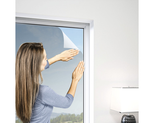 Une femme pose un film de protection visuelle sur une fenêtre