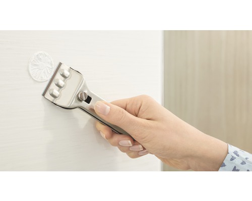 Une main tient un grattoir à vitre pour enlever des résidus d''une surface.