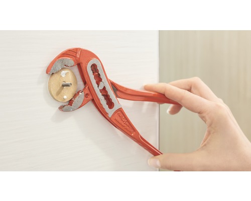 Une personne utilise une pince multiprise pour visser une cheville en bois avec une vis dans une surface blanche.