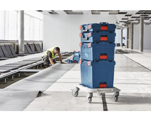 Caisses à outils empilables sur un plateau à roulettes dans un chantier avec un ouvrier