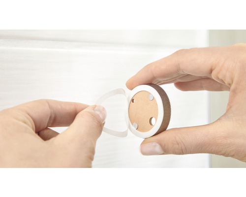 Une main retire le film protecteur d''un bouton de meuble rond pour le montage.