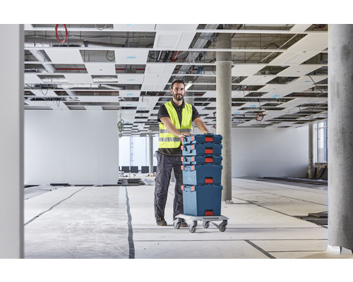 Artisan avec des boîtes à outils sur une planche à roulettes dans un bâtiment brut.