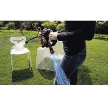 Une personne utilise un nettoyeur haute pression sans fil dans le jardin pour nettoyer une chaise. Une bouteille d''eau est connectée au nettoyeur haute pression.