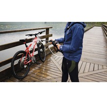 Une personne nettoie un vélo avec un nettoyeur haute pression portable sur un pont en bois près d''un point d''eau.