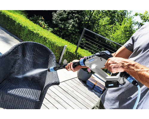 Eine Person reinigt einen Korbstuhl mit einem Gloria Hochdruckreiniger im Außenbereich.