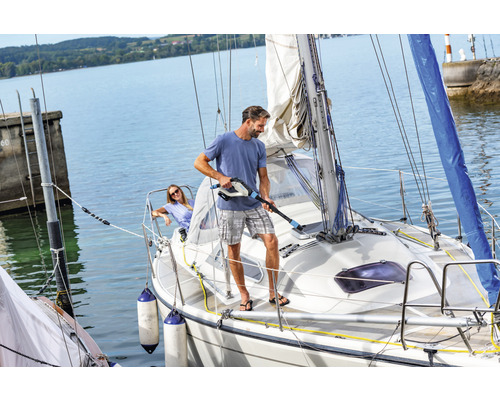 Mann reinigt ein Segelboot mit einem tragbaren Reinigungsgerät auf dem Wasser.