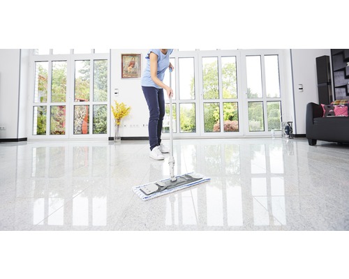 Femme essuyant le sol avec un balai à franges dans une pièce lumineuse avec de grandes fenêtres