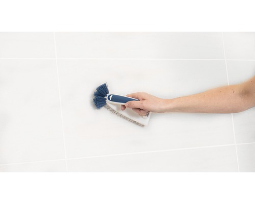 Une main tient une brosse pour nettoyer les joints de carrelage.