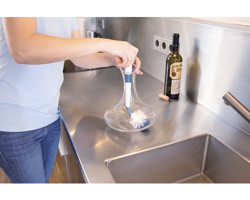 Une personne nettoie une carafe en verre avec une brosse de nettoyage dans la cuisine.