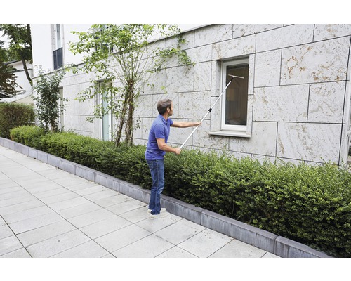 Un homme nettoie une fenêtre avec un lave-vitre sur une perche.