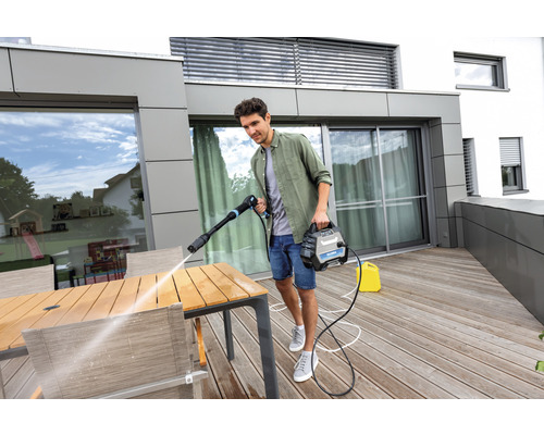 Mann reinigt Gartentisch mit Hochdruckreiniger auf Terrasse