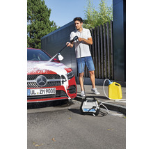 Ein Mann reinigt ein Auto mit einem Hochdruckreiniger, während ein gelber Wasserkanister und das zugehörige Gerät daneben stehen.