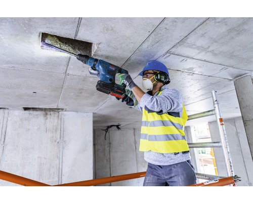 Un ouvrier perce un trou dans un plafond en béton avec un marteau perforateur.
