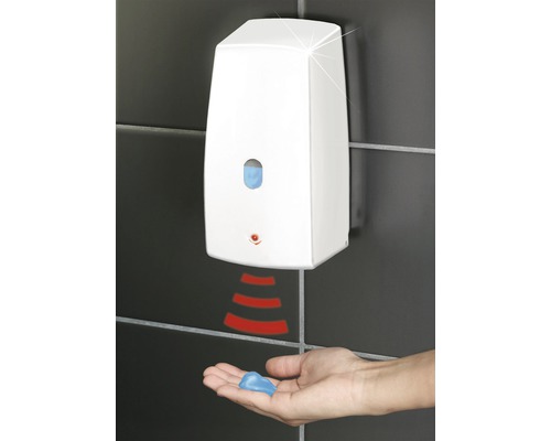 Automatischer Seifenspender an einer gefliessten Wand mit einer Hand darunter, die Seife auffängt.