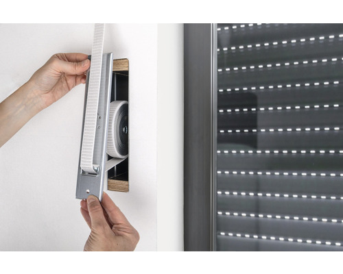 Une personne installe un enrouleur de sangle de volet roulant au mur à côté d''un volet roulant.