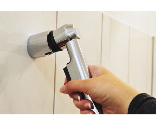 Main tenant une douchette de bidet en métal sur un support mural
