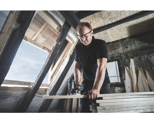 Artisan travaillant avec une défonceuse dans des combles.