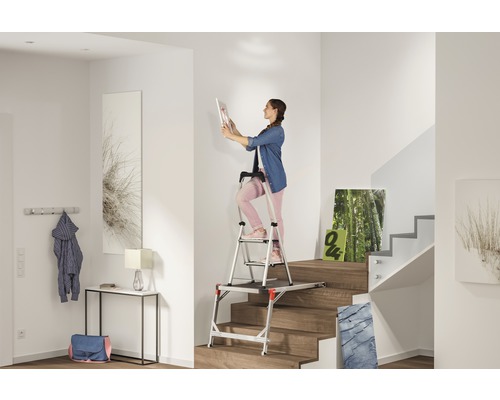 Femme sur un escalier à plateforme dans une cage d''escalier lumineuse, accrochant un tableau
