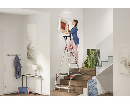 Femme accrochant une photo avec un escabeau dans le couloir