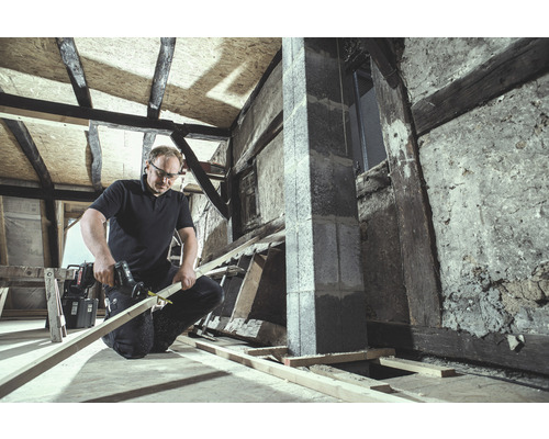Handwerker sägt Holz mit einer Säbelsäge in einem unrenovierten Raum.