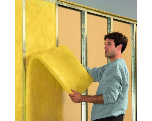 Un homme fixe de la laine minérale jaune sur un mur avec ossature métallique.