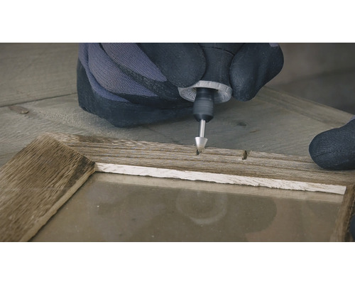 Une personne portant des gants utilise un outil multifonction sur un cadre en bois.