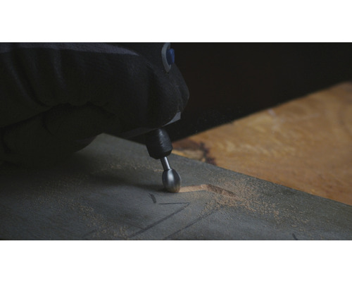 Une personne utilise un outil multifonction pour sculpter un morceau de bois.