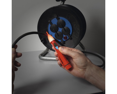 Testeur de tension dans la main devant un enrouleur de câble