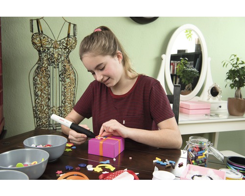 Junge Frau dekoriert Geschenk mit Klebepistole und Dekomaterialien