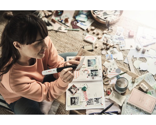 Frau benutzt Bosch Klebestift zum Basteln an Scrapbook mit Fotos und Dekorationen