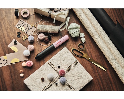 Dekorativ gestaltete Geschenke und Bastelutensilien auf einem Tisch, darunter ein Bosch Klebestift