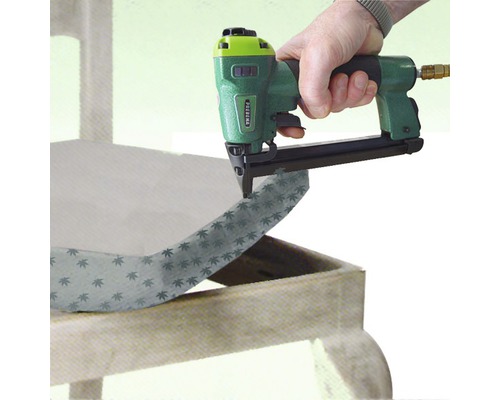 Eine Person benutzt einen Druckluftnagler, um Stoff an einem Möbelstück zu befestigen.