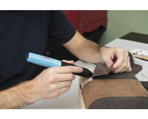 Une personne utilise un stylo à colle Bosch Gluey pour fixer du tissu sur du bois