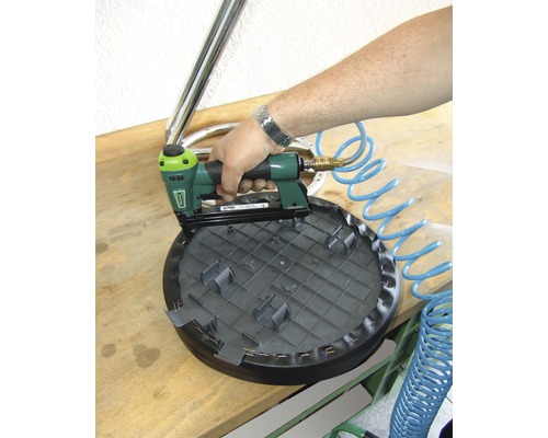 Person befestigt Bezug mit Druckluftnagler an einem Hocker