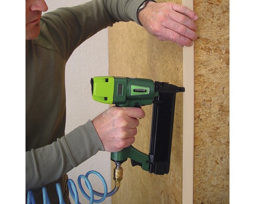 Eine Person befestigt eine Holzleiste mit einem Druckluftnagler an einer Holzwand.