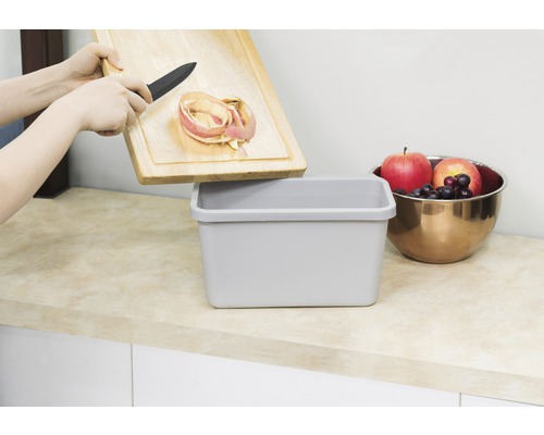 "Une personne jette des épluchures de pommes d''une planche à découper en bois dans une poubelle 