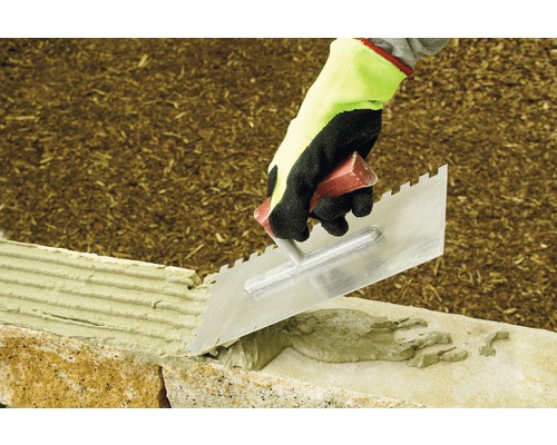 Artisan utilisant une truelle pour poser des pierres.