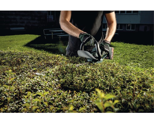 Eine Person schneidet eine Hecke mit einer Heckenschere.