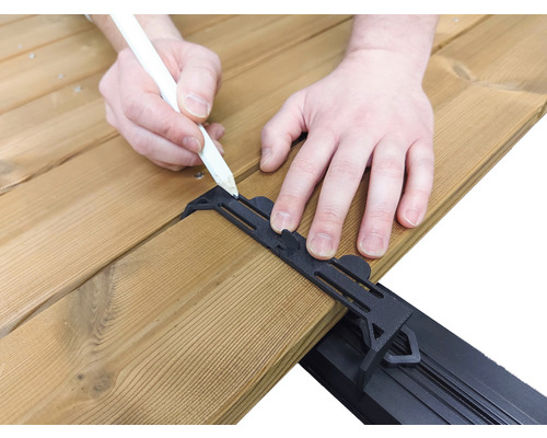 Eine Person zeichnet mit einem Stift auf eine Holzterrasse mit einer schwarzen Abstandshalterung.