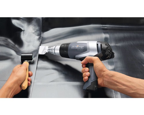 Une personne utilise un décapeur thermique Steinel HG 2320 E et un rouleau de pression pour le traitement de membranes de toiture.